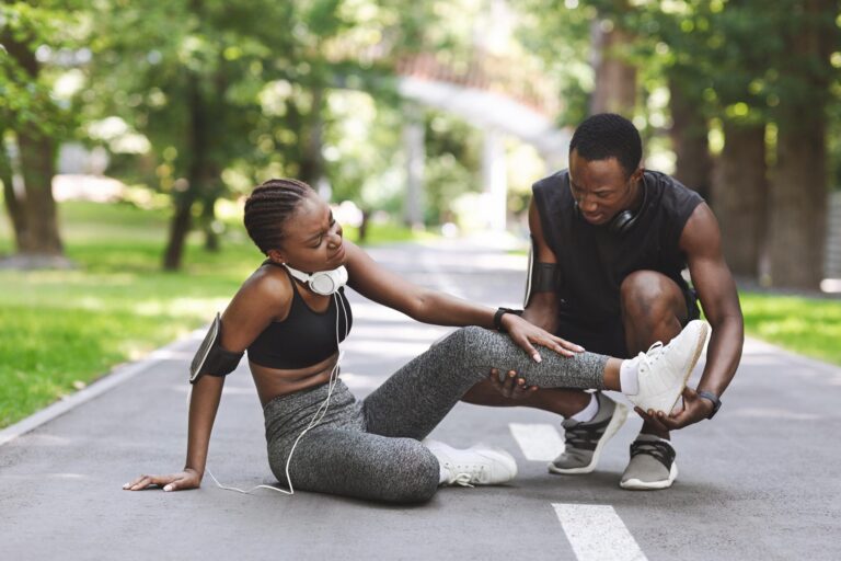 A woman lying down looking to be injured on her calf and a man checking up on her.