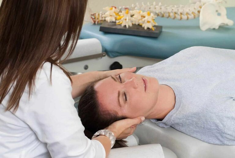 A woman being threated in her neck from a chiropractor while lying face up on a massage bed.