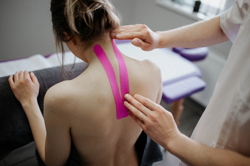 A woman having adhesive supporting bandages applied on her neck by a specialist.