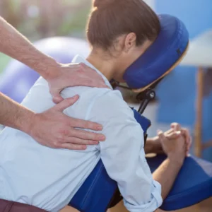 A woman lying on a massage seat and having treatment to her shoulder.