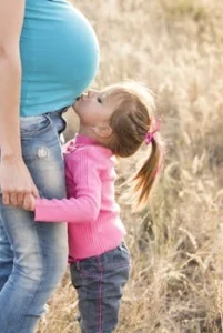 A child kissing the belly of a pregnant woman.