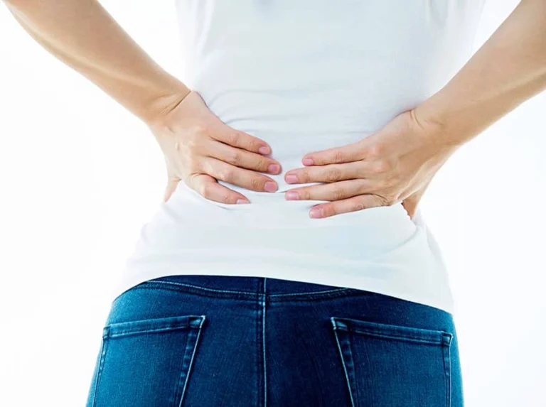 A woman touching her lower back with both hands.