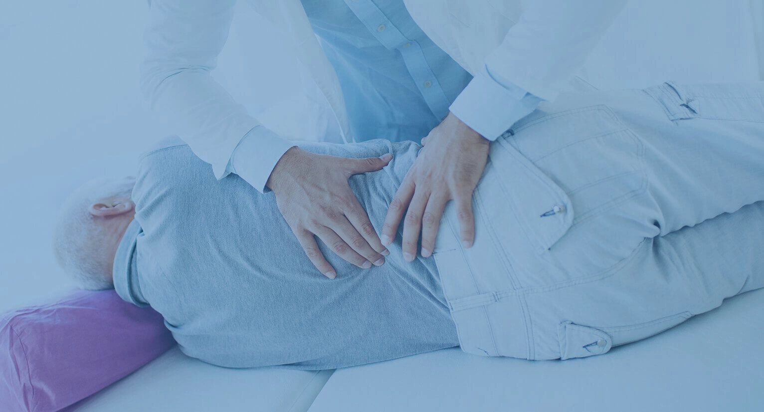 An elderly man receiving care in his lower back by a chiropractor while lying on his side.