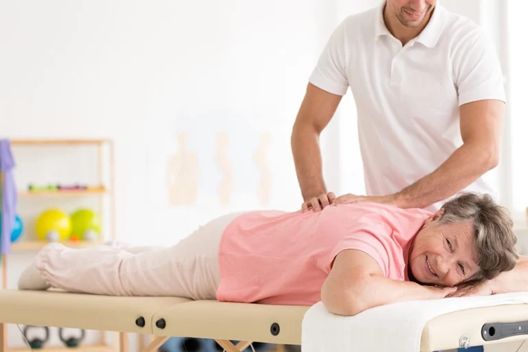 An older woman having chiropractic treatment on her back and smiling.