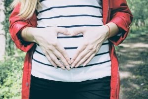 A woman making a heart gesture in front of her belly.