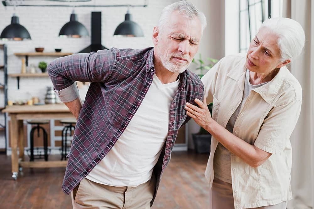 A man trying to stand up while feeling pain in his lower back and a woman trying to help him.