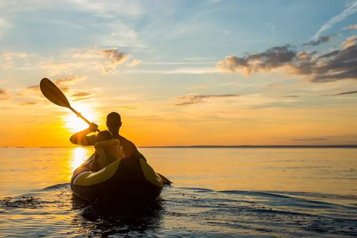 A man rowing with a child in the sunset.