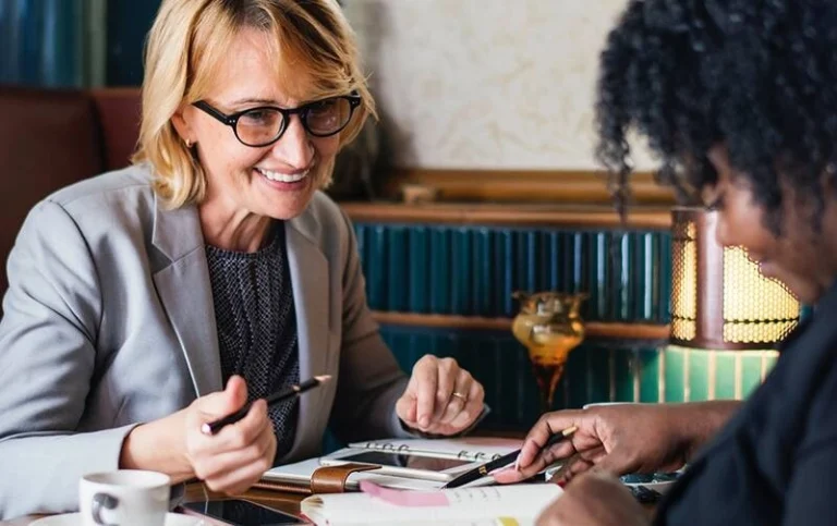 Two women discussing on a table with their agendas.