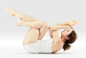 A woman doing a yoga pose in a white room with white clothes.