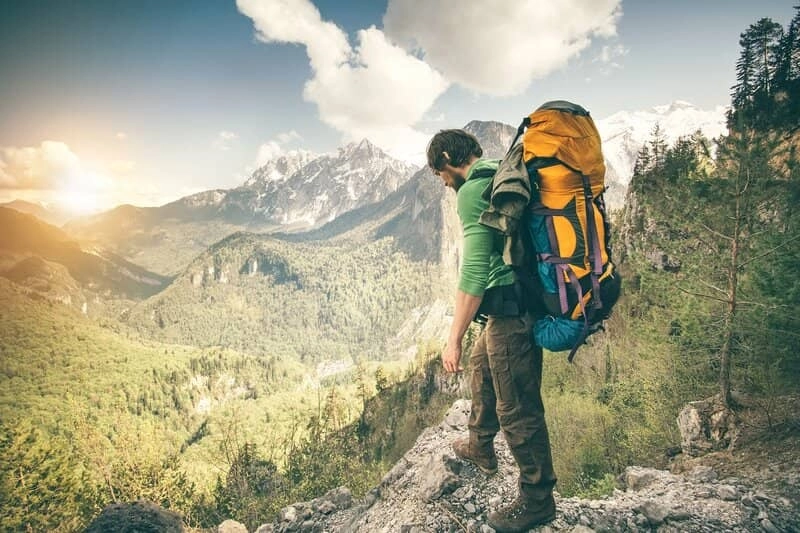 A hiker loaded with a heavy backpack, looking at a forest and mountains view.