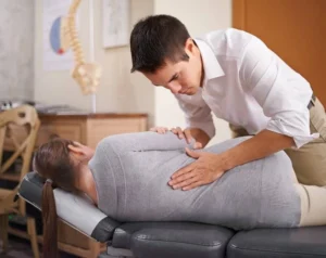 A young chiropractor treating the back of a female patient.