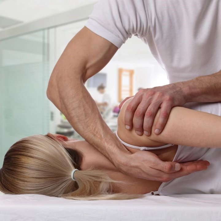 A woman having her shoulder treated by a chiropractor, while lying on a massage table.