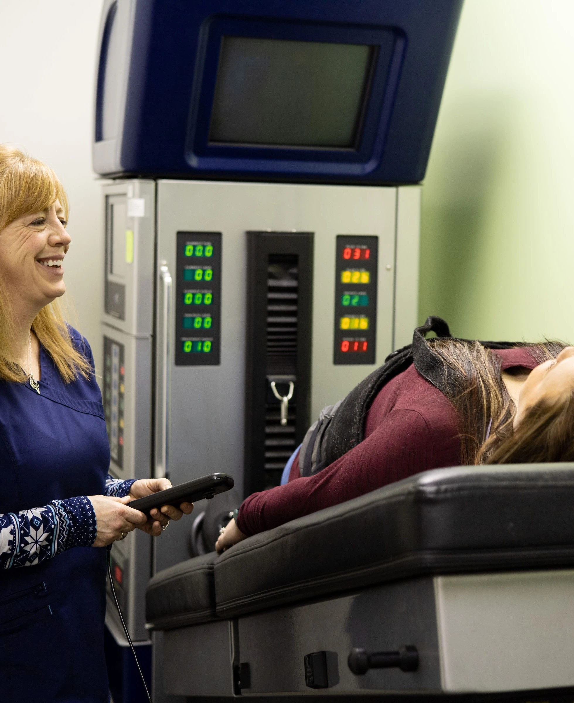 A member of Better Health Alaska chatting with a patient while facilitating the use of a DRS System machine for that patient.