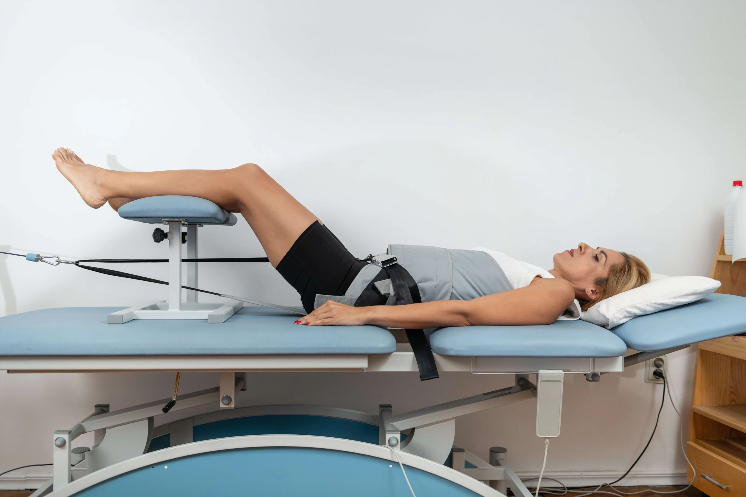 A woman lying face up in a machine made to pull the legs in order to achieve spinal decompression.