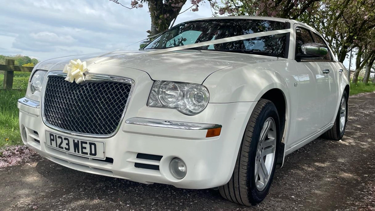 Front Left view of a White Chrysler 300c Saloon with White ribbons and bow across the front bonnet